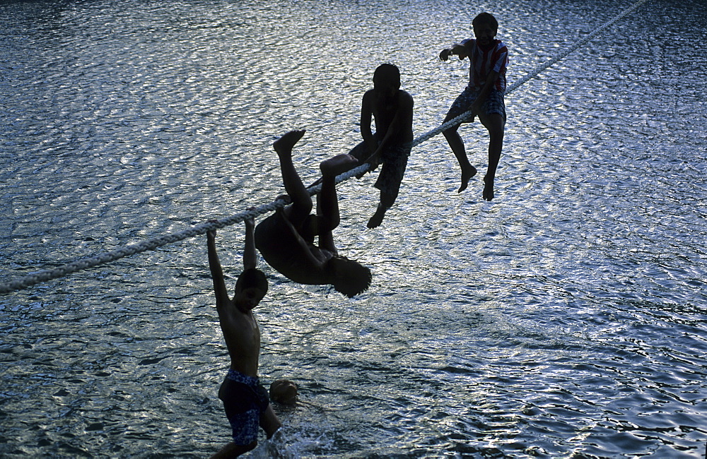 Children playing on a rope in the harbour of Hakahau on the island of Ua Pou, French Polynesia