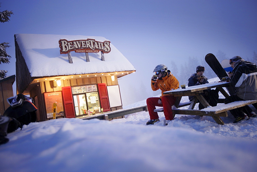 Skiers and snowboarders resting beside snack stall, Grouse Mountain, British Columbia, Canada