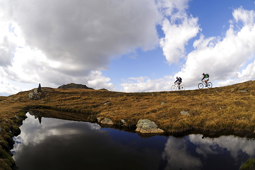 People on mountain bikes at mountain lake under clouded sky, Markinkele, Innichen, Val Pusteria, Dolomites, South Tyrol, Italy, Europe