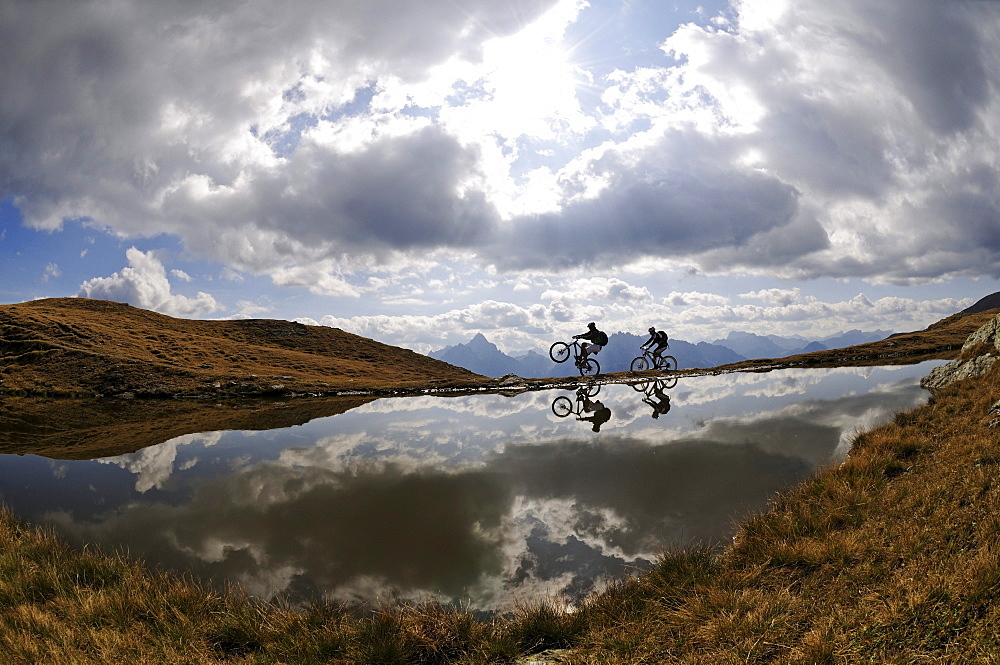 People on mountain bikes at mountain lake under clouded sky, Markinkele, Innichen, Val Pusteria, Dolomites, South Tyrol, Italy, Europe