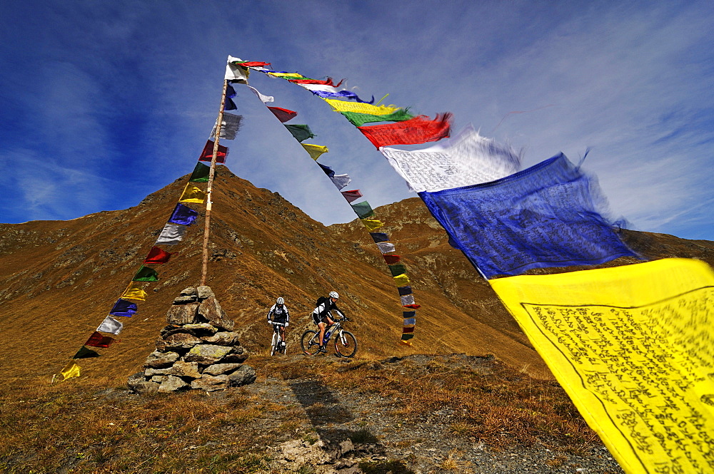 People on mountain bikes at Karnischer Hoehenweg next to prayer flags, Dolomites, South Tyrol, Italy, Europe