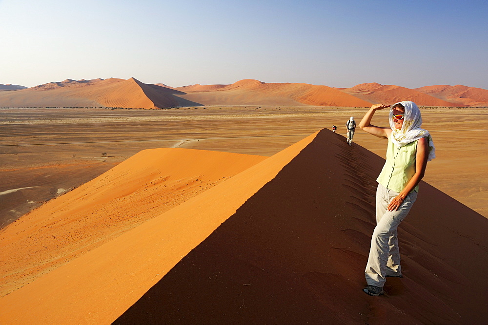 Woman standing on red sand dune and enjoying view in Sossusvlei, dune 45, Sossusvlei, Namib Naukluft National Park, Namib desert, Namib, Namibia