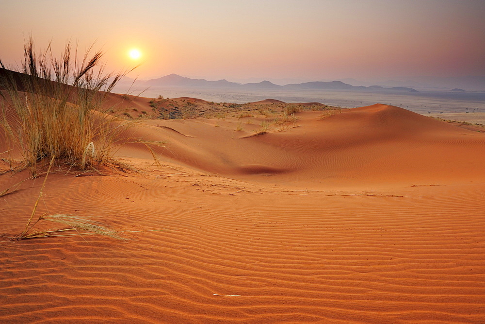 Sunrise over red sand dunes with Tiras mountains in background, Namib Rand Nature Reserve, Namib desert, Namib, Namibia