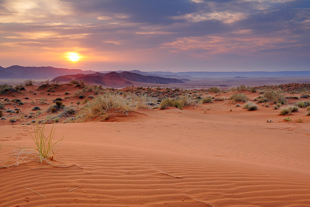 Sunrise over red sand dunes with Tiras mountains in background, Namib desert, Namibia