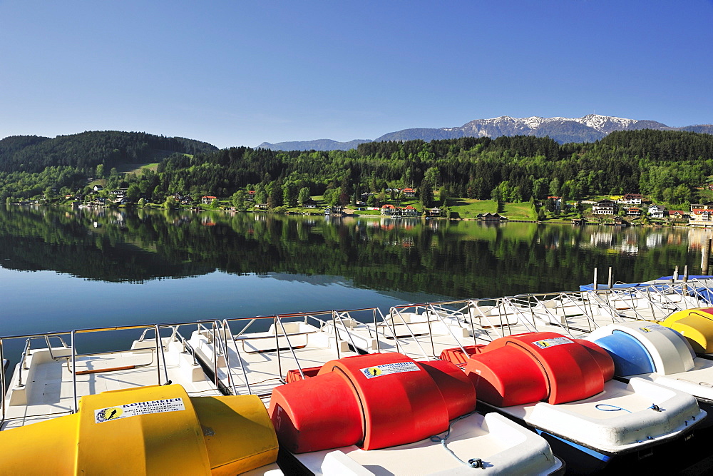 Multicolored pedal boats at lake Millstaetter See with snow covered mountains in the background, Seeboden, lake Millstaetter See, Carinthia, Austria, Europe