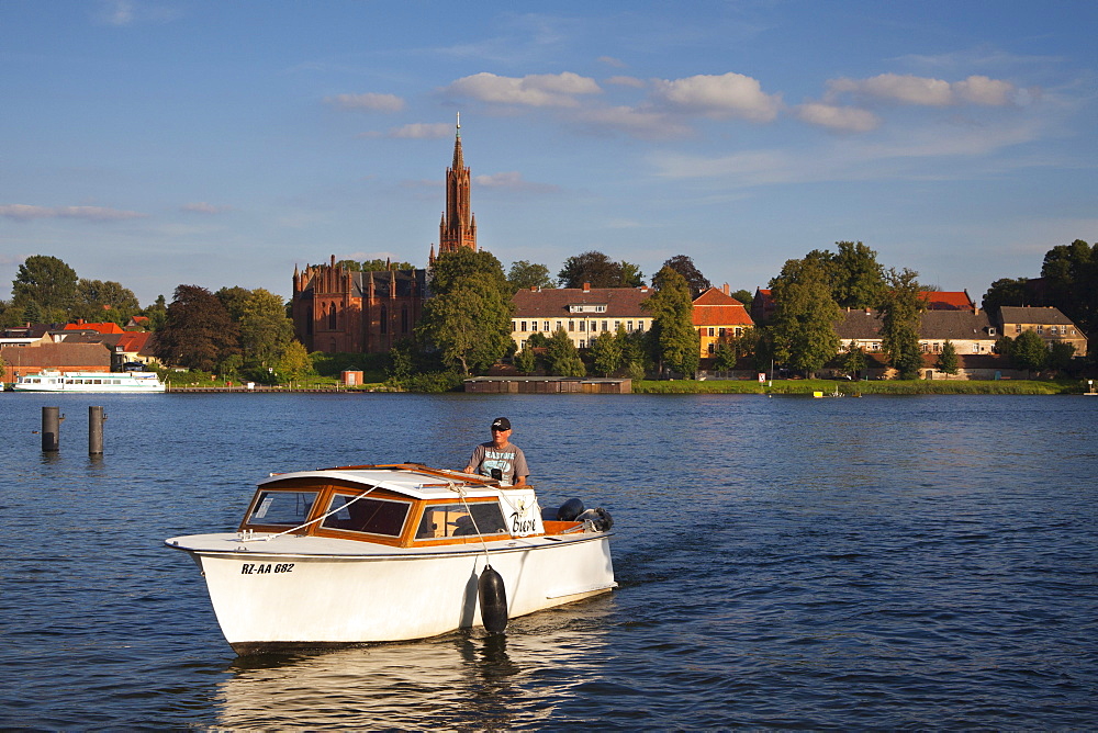 Fisherman in motorboat, view over Fleesensee lake to Malchow monastery, Mueritz-Elde-canal, Mecklenburg lake district, Mecklenburg Western-Pomerania, Germany, Europe