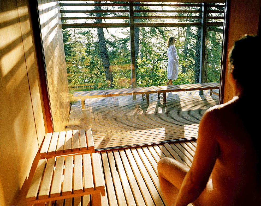 Man sitting in a sauna, woman standing outside on terrace, Vigilius Mountain Resort, Vigiljoch, Lana, Trentino-Alto Adige/Suedtirol, Italy