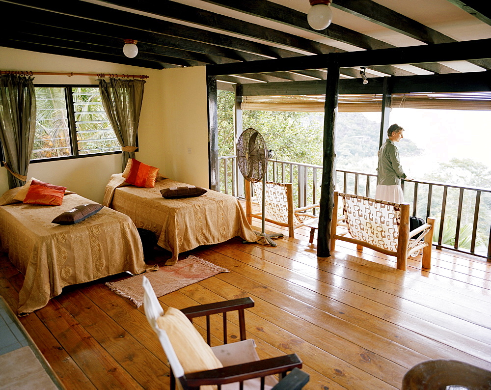 Woman on balcony of Superior Room Chalet, Mango Lodge, view over Anse Volbert, Bahia Ste. Anne, Praslin, Republic of Seychelles, Indian Ocean