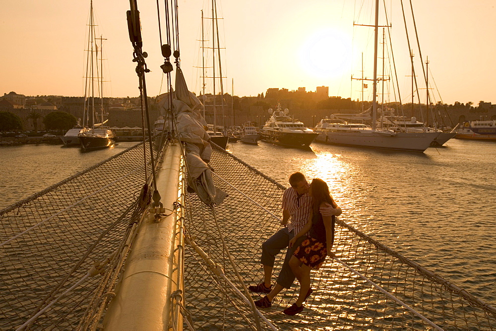 Couple in Bowsprit Net, Star Flyer, sunset over the Rhodes Harbor, Rhodes, Dodecanese Islands, Greece