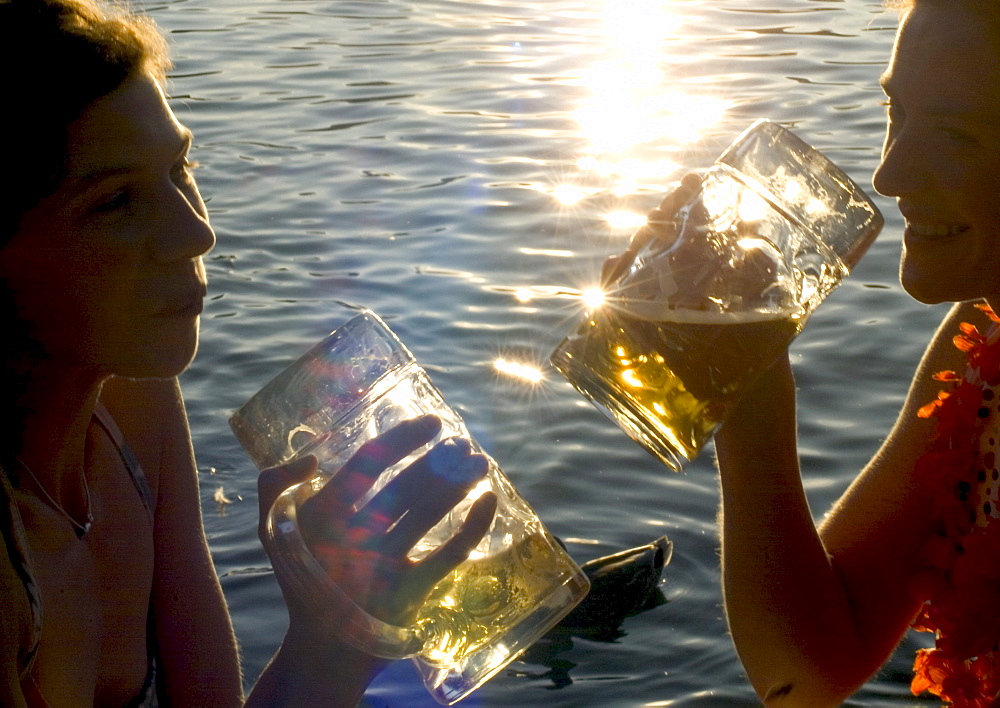 Young women toasting with beer steins, Seehaus Beergarden, English Garden, Munich, Bavaria, Germany