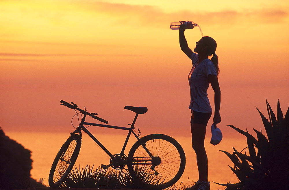 Female mountainbiker cooling herself with water after cycling tour, coastline, Mallorca, Spain