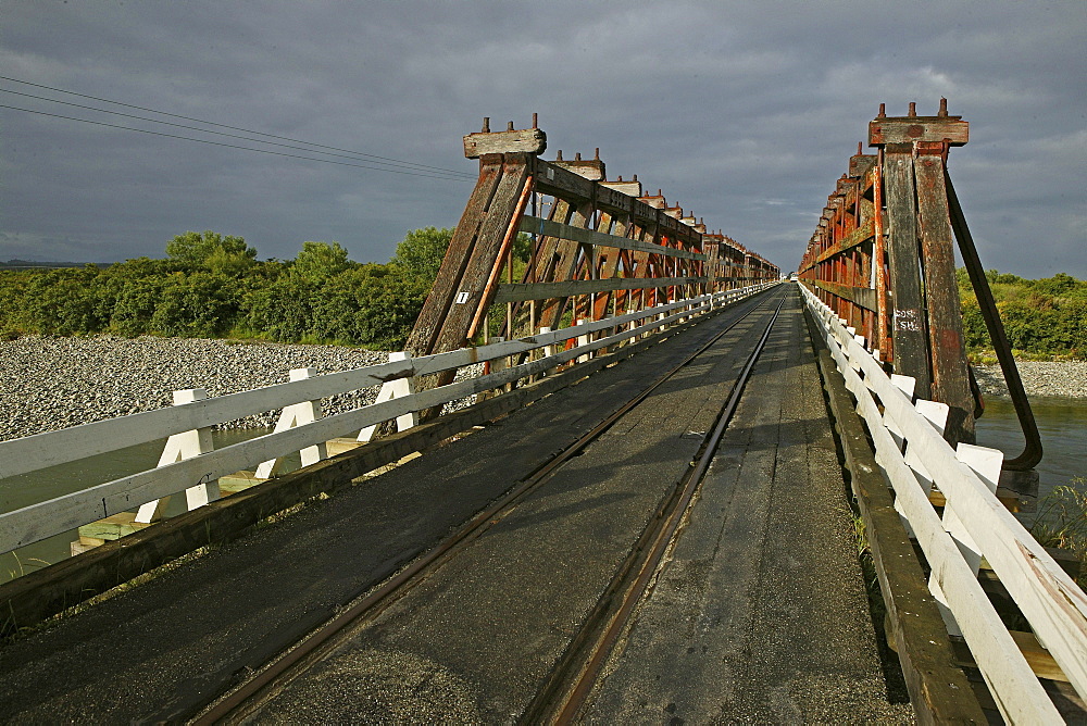 Wooden bridge under clouded sky, traffic and railway sharing the narrow bridge, West Coast, South Island, New Zealand, Oceania