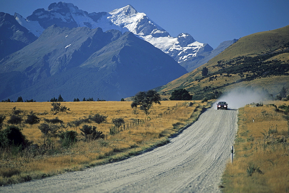 Country road with car in front of snowy mountains, Central Otago, South Island, New Zealand, Oceania