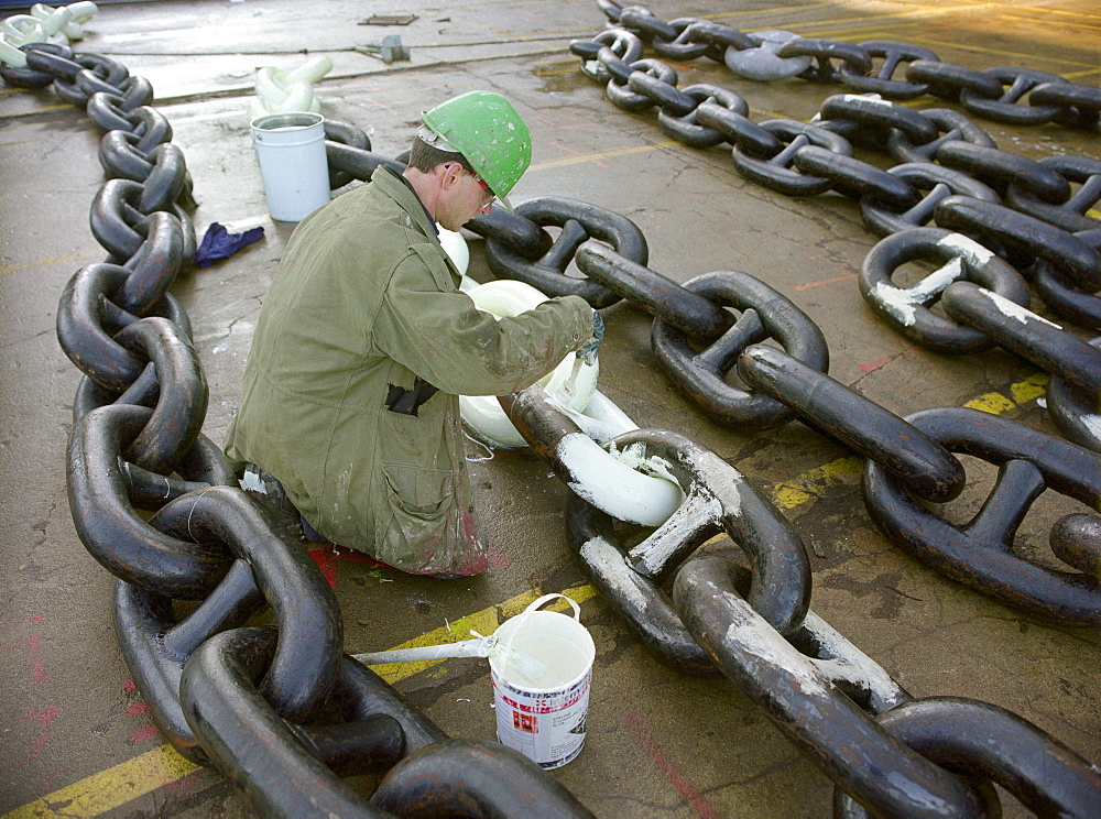 Worker painting the anchor chain white, dry dock, Queen Mary 2, Saint-Nazaire, France