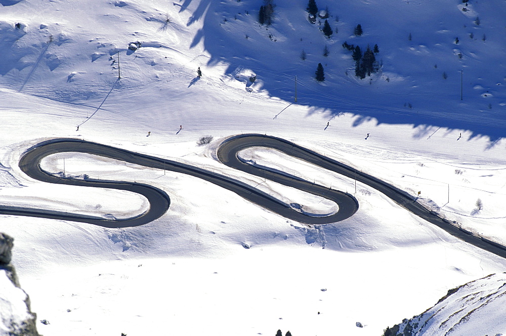 People skiing on a ski slope next to a serpentine, Passo Pordoi, South Tyrol, Italy