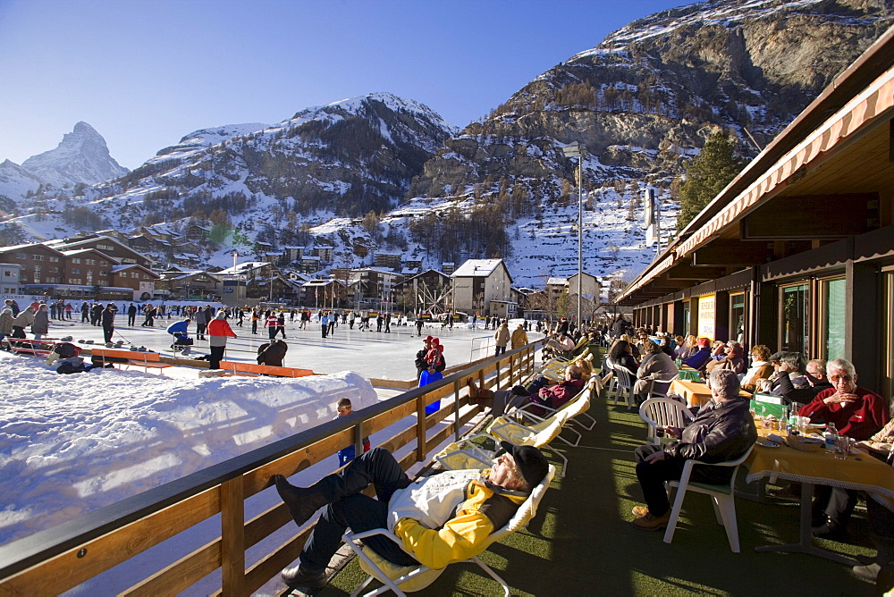 Visitors enjoying a curling game, Matterhorn in background, Zermatt, Valais, Switzerland (Curling: A rink game where round stones are propelled by hand on ice towards a tee (target) in the middle of a house (circle)).