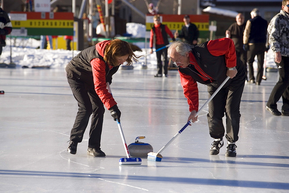 Man and woman curling on a rink, Zermatt, Valais, Switzerland (Curling: A rink game where round stones are propelled by hand on ice towards a tee (target) in the middle of a house (circle)).