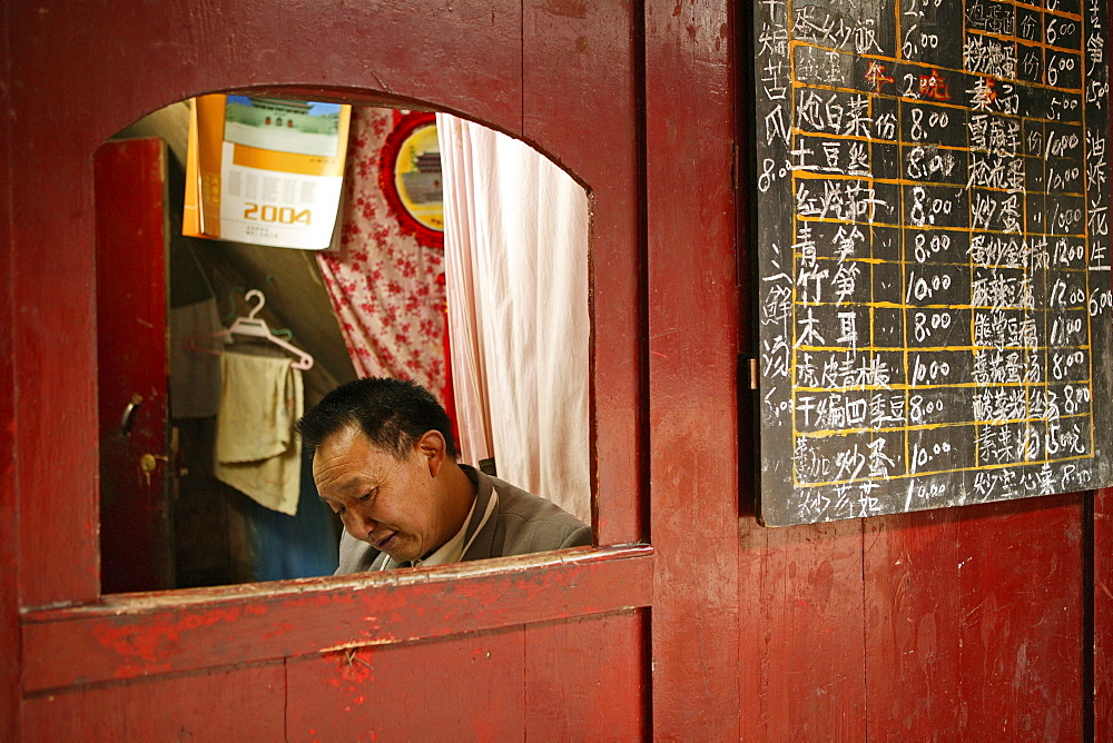 Man sitting in a booth next to the menu, canteen of the Xixiang Chi monastery, Emei Shan, Sichuan province, China, Asia