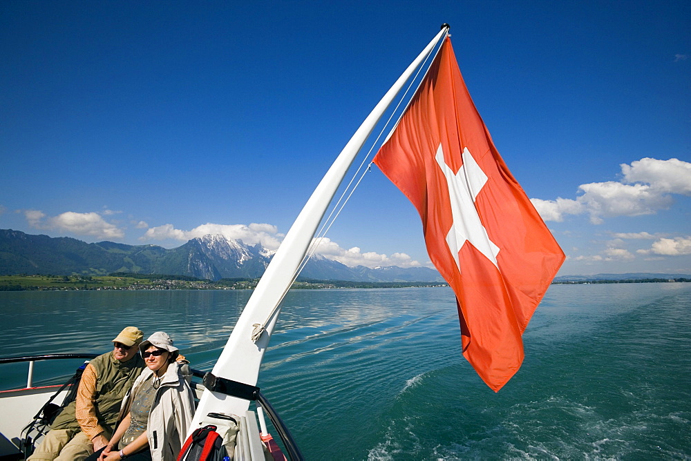 Couple sitting at stern of a ship, swiss flag blowing in the wind, Lake Thun, Bernese Oberland (highlands), Canton of Bern, Switzerland