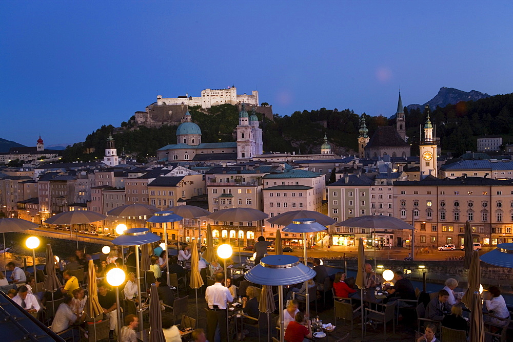 View over illuminated roof deck of restaurant Hotel Stein to old town with Salzburg Cathedral, St. Peter's Archabbey, Franciscan Church, City Hall Tower and Hohensalzburg Fortress, largest, fully-preserved fortress in central Europe, in the evening, Salzburg, Salzburg, Austria, Since 1996 historic centre of the city part of the UNESCO World Heritage Site