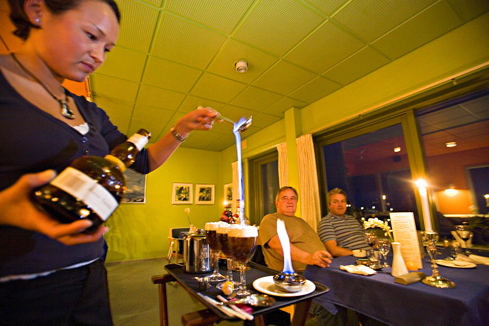 A waitress serves greenland coffee at Qaqortoq former Julianehab), the burning alcohol simbolizes the aurora borealis, the white cream the ice and the coffee the soil, South Greenland.