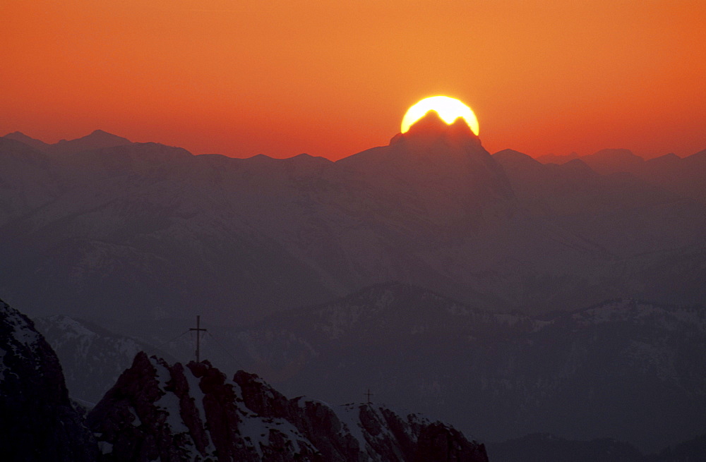 sun behind summit of Guffert with pinnacles with crosses on summit in foreground, Kaiser range, Tyrol, Austria