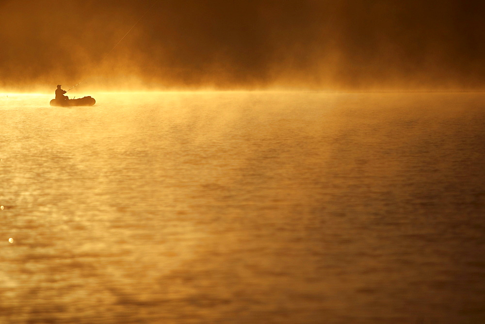 Man is fishing and sitting in a boot, Fuessen, Bavaria, Germany