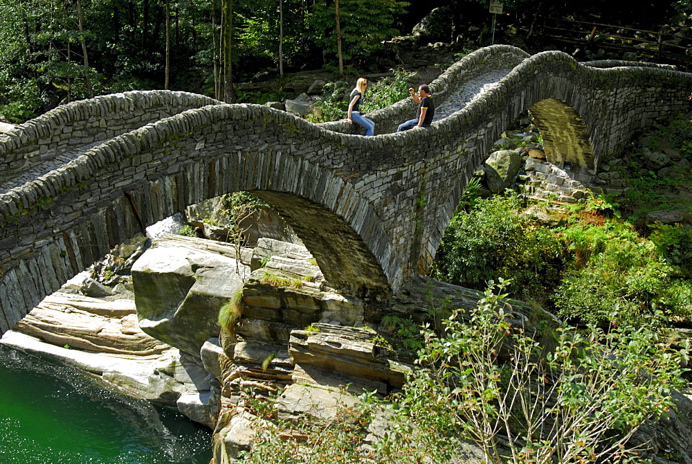 couple sitting on bridge crossing Verzasca, Lavertezzo, Ticino, Switzerland