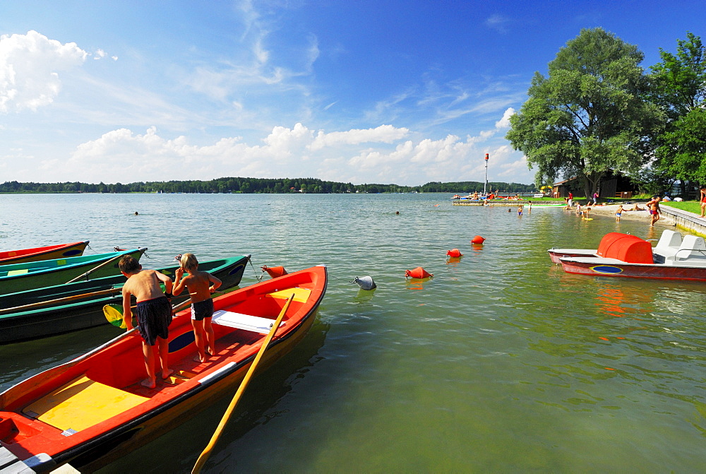 Two children fishing on rowing boat at beach of lake Simssee, Chiemgau, Upper Bavaria, Bavaria, Germany