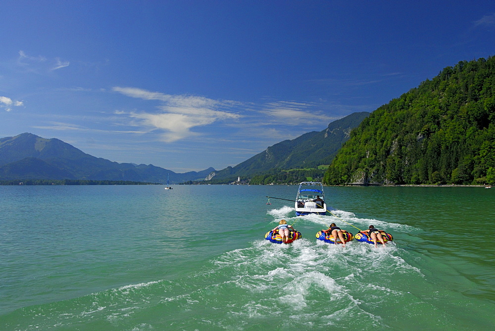 three young women tube riding behind motor boat, lake Abersee, lake Wolfgangsee, Salzkammergut, Salzburg, Austria