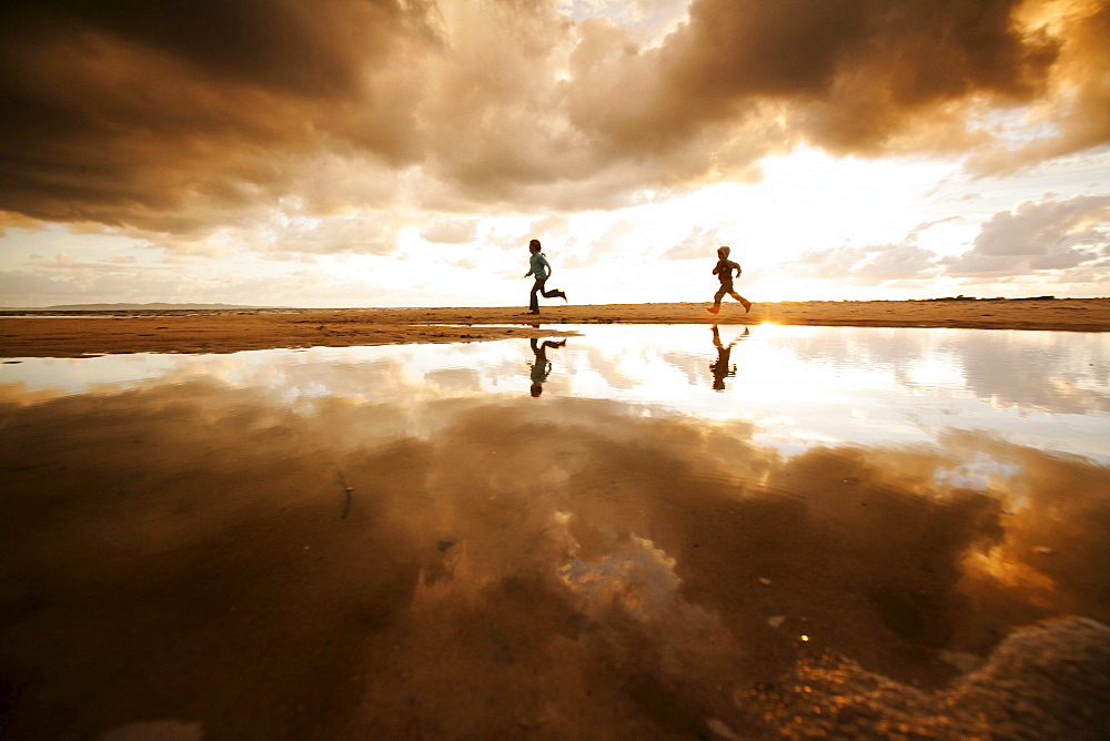 Two children running along the beach on a cloudy day, Reflection, Segeltorpstrandet, Halmstadt, Skane, Sweden