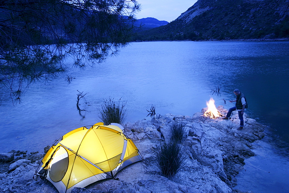 Man grilling fish on camp fire, camping on small island on lake, dusk, Valencia region, Spain