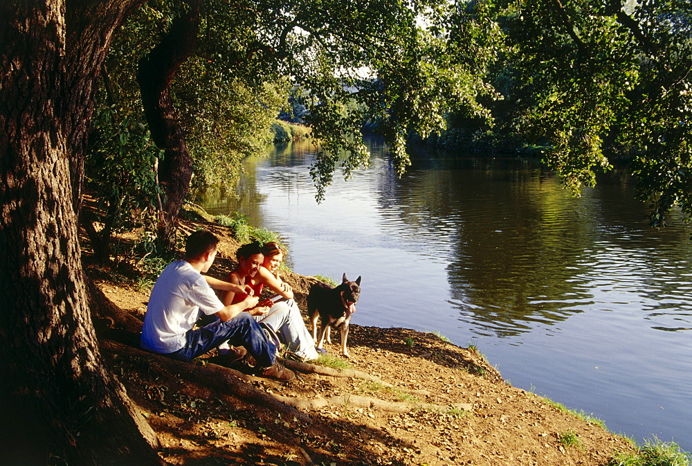Three young people and a dog having a picnic near river, Witten, Ruhr Valley, Ruhr, Northrhine Westphalia, Germany