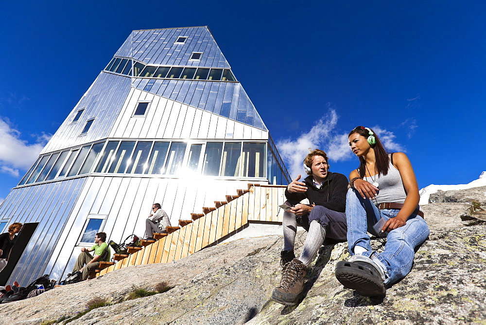 Two young people with headphones in front of New Monte Rosa Hut, myclimate audio trail, Zermatt, Pennine Alps, Canton of Valais, Switzerland