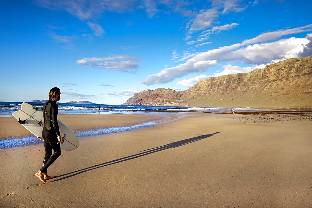 Surfer on the beach, Playa de Famara, mountain range Risco de Famara, Lanzarote, Canary Islands, Spain, Europe