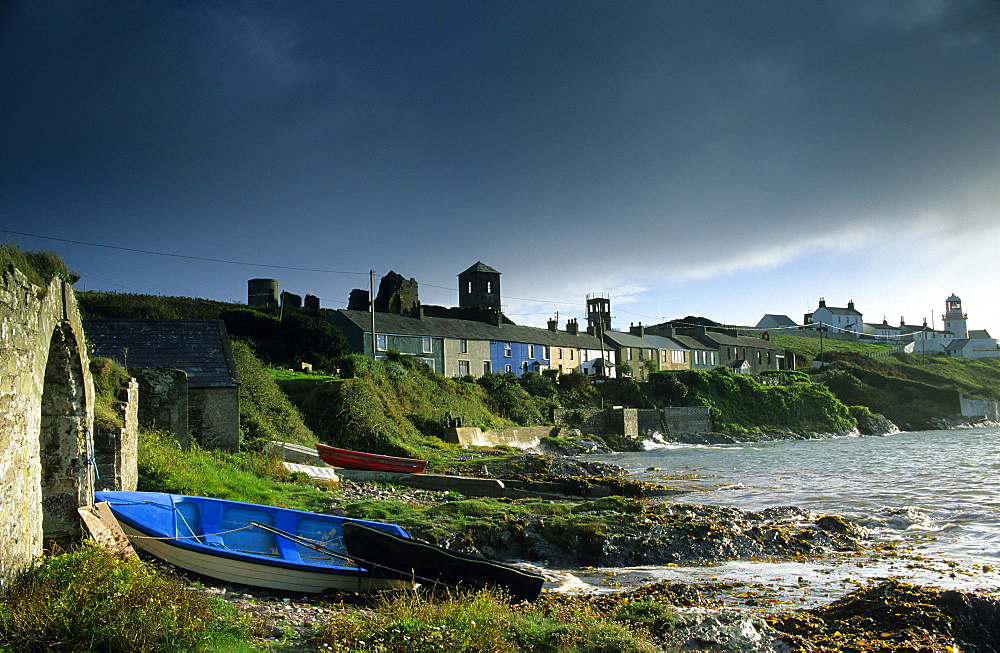 Houses and lighthouse on shore under thunder clouds, Roche's Point, County Cork, Ireland, Europe