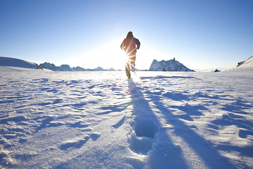 Man running over glacier towards sunrise, overlooking Les Grandes Jorasses and Dent du Geant, Chamonix Mont Blanc, France, Europe