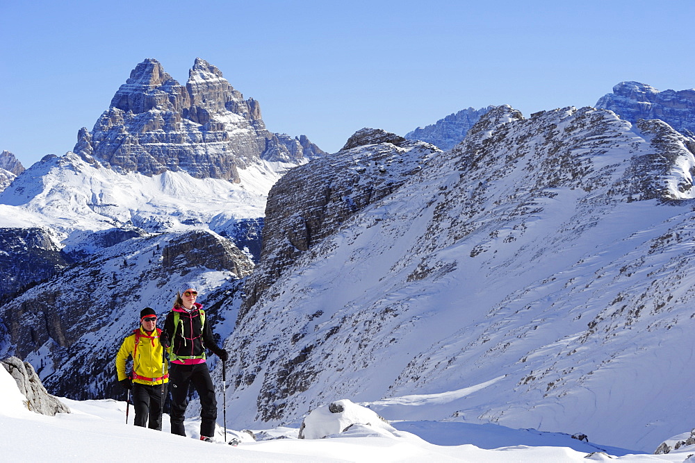 Young woman and young man ascending with crosscountry skis to Corno d'Angolo, Tre Cime di Lavaredo in background, Corno d'Angolo, Cortina, Veneto, Dolomites, Italy, Europe