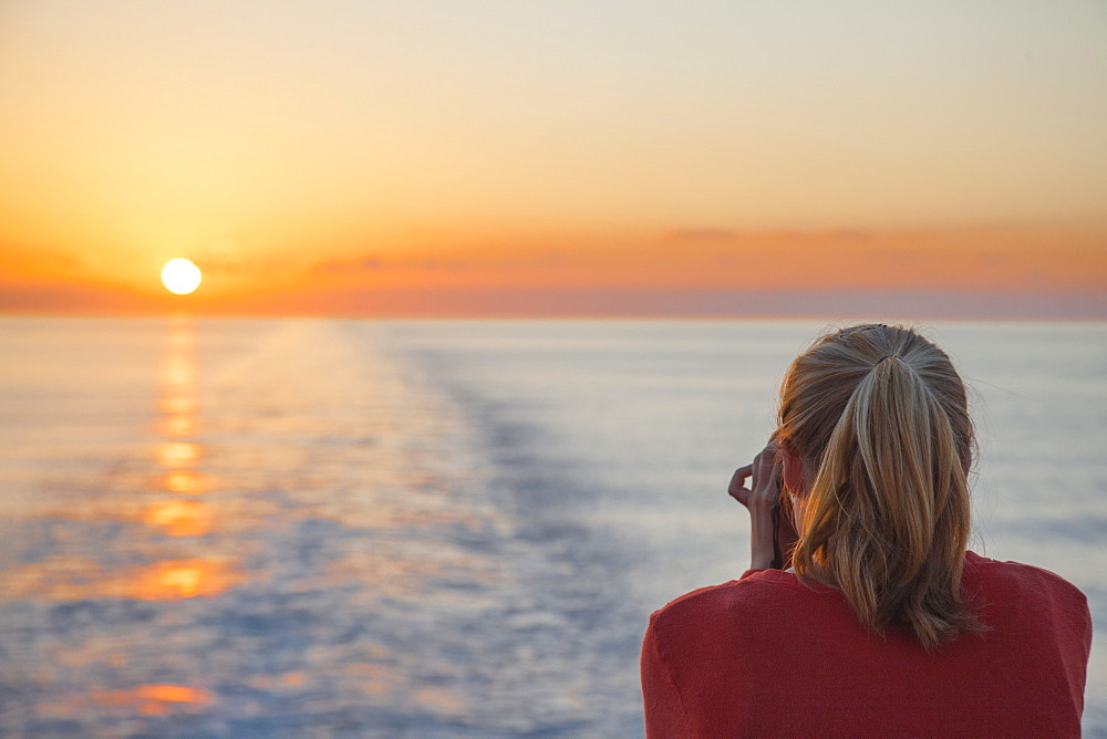 Young woman taking photographs of the sunset from cruise ship MS Deutschland (Reederei Peter Deilmann), Caribbean Sea, near Cayman Islands