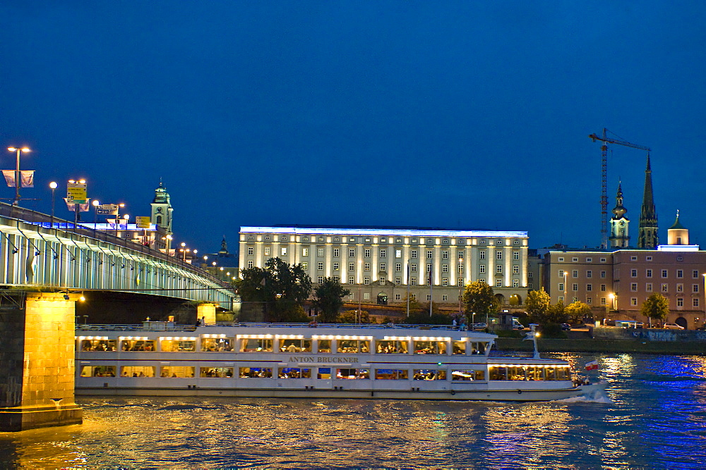 An excursion boat driving on the Danube at night, University of Art in the background, Linz, Upper Austria, Austria