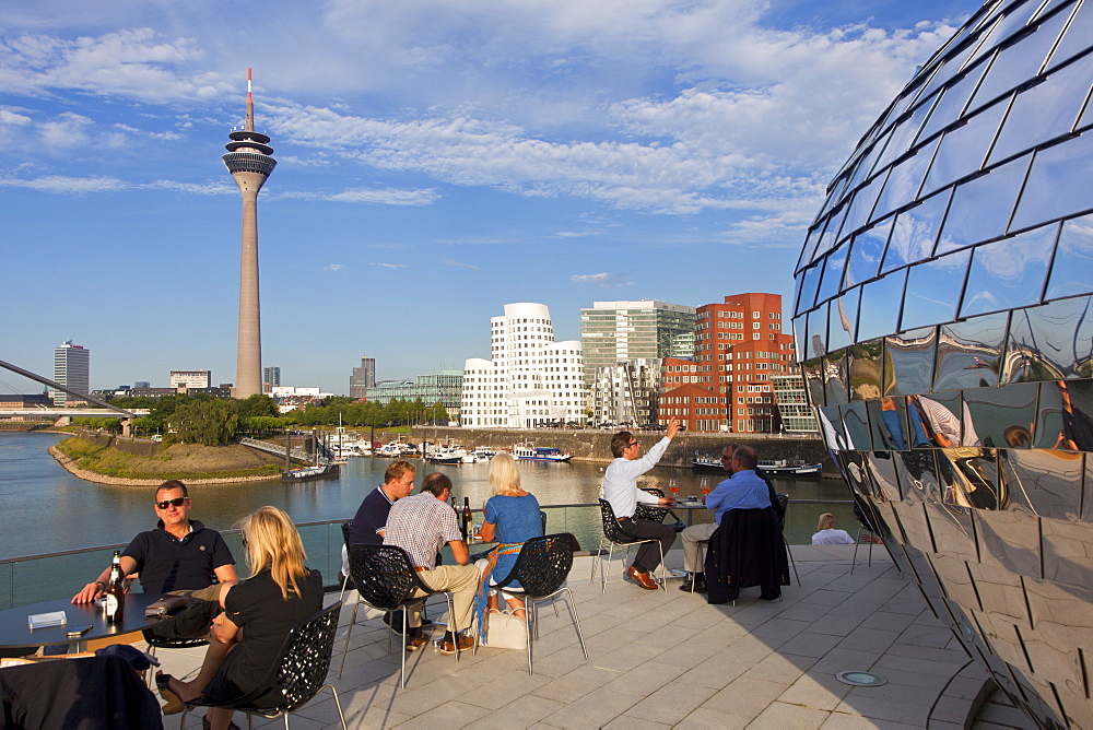 People at the terrace of a restaurant at media harbour, view to Rhine tower and Neuer Zollhof, Duesseldorf, North Rhine-Westphalia, Germany, Europe