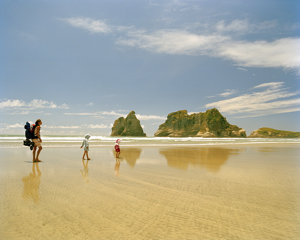 Mother with children hiking through shallow water, Wharariki Beach, northwest coast, South Island, New Zealand