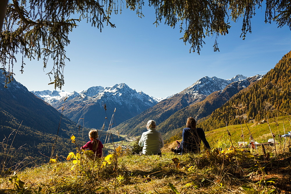 A family, two girls, a younger and an older woman sit on a meadow, autumn at Guarda, Engadin, Graubuenden, Grisons, Switzerland