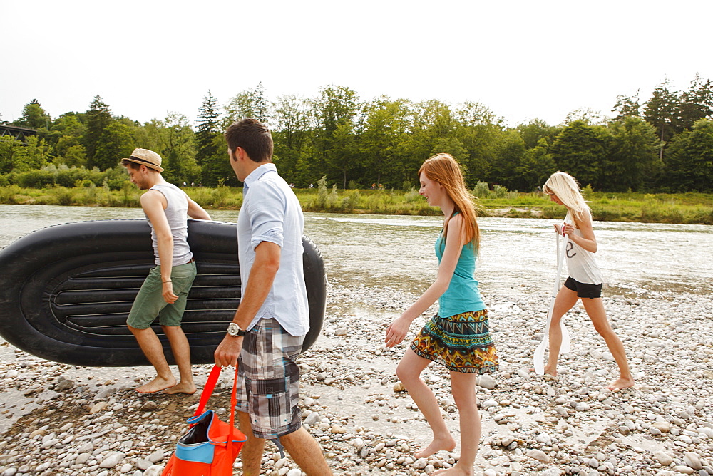 Young people with a rubber dinghy on the Isar riverbank, Munich, Bavaria, Germany