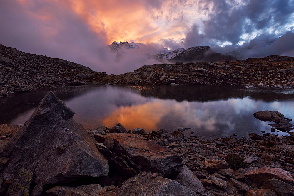 Dramatic play of light in a small mountain lake below Piz Langalb with Bernina mountain range in the background, Engadin, Switzerland