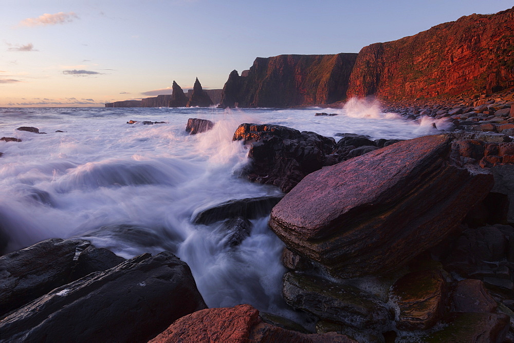 Impressively illuminated red, wild coast of Duncansby Head on the northeastern coast of Scotland with the Duncansby Stacks in the background, United Kingdom