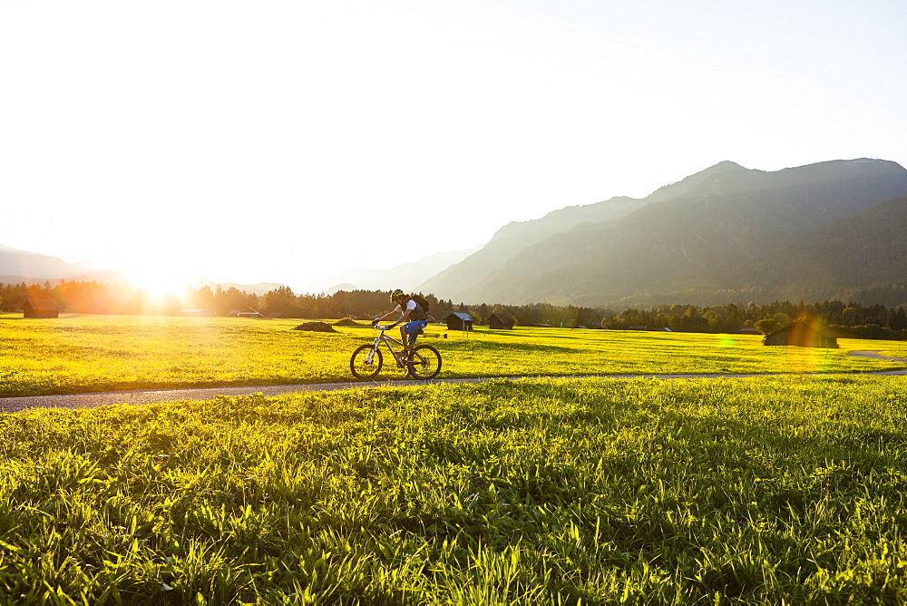 Mountain biker passing meadow with hay barns, Grainau, Bavaria, Germany