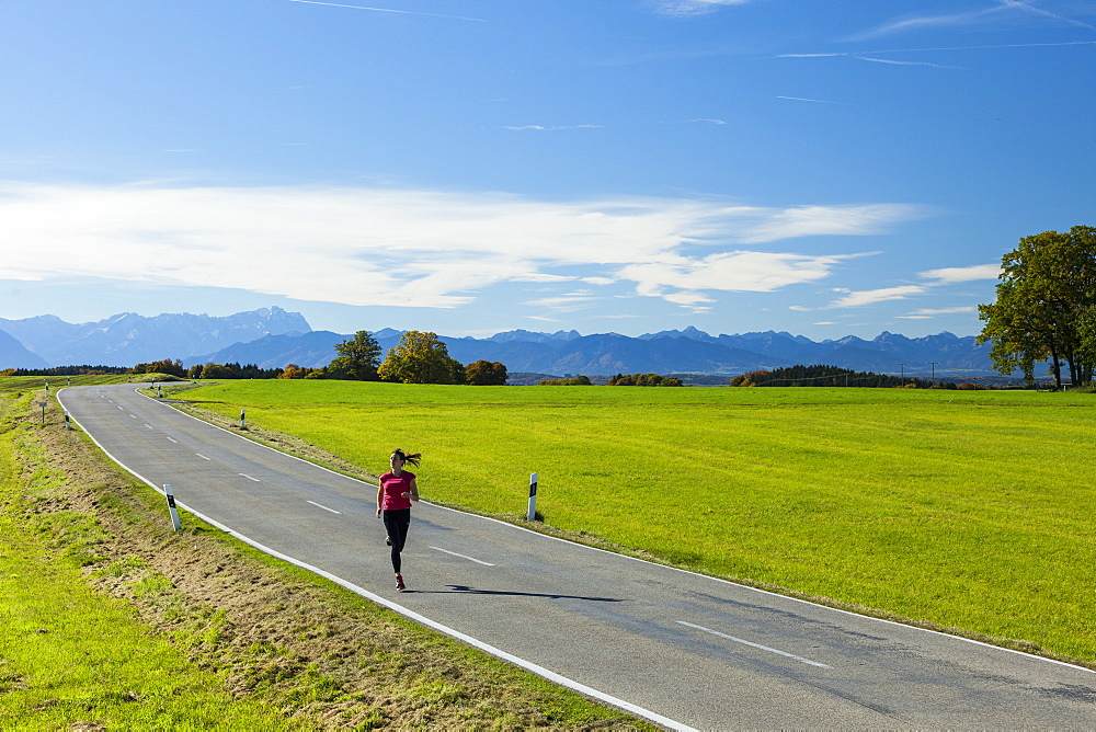 Woman jogging along a road, Munsing, Bavaria, Germany