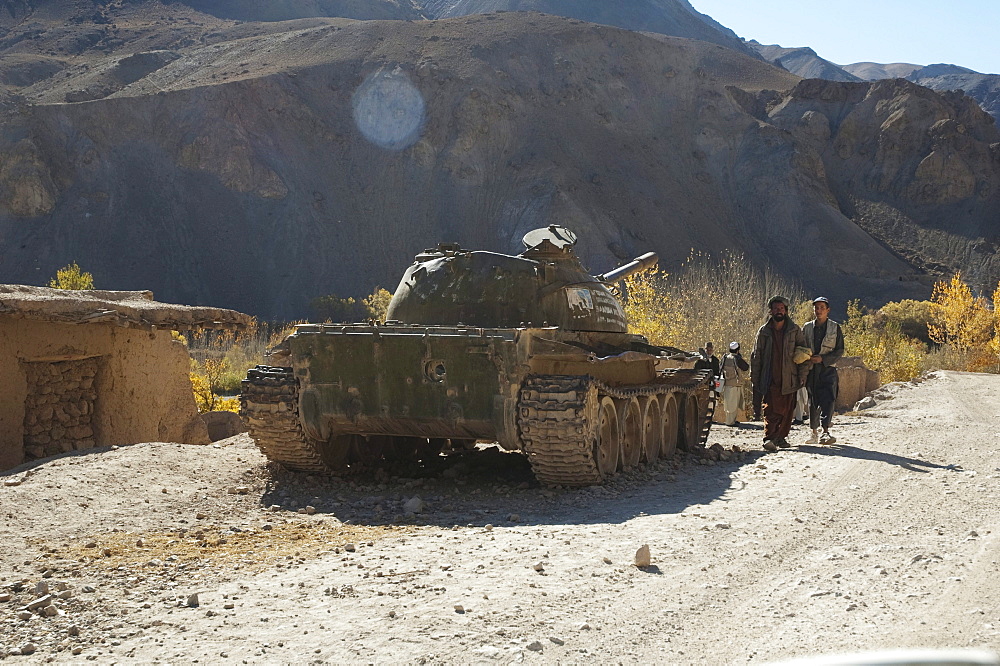 Afghan men walk by an abandoned Soviet tank in Shekh Ali, Parwan Province, Afghanistan