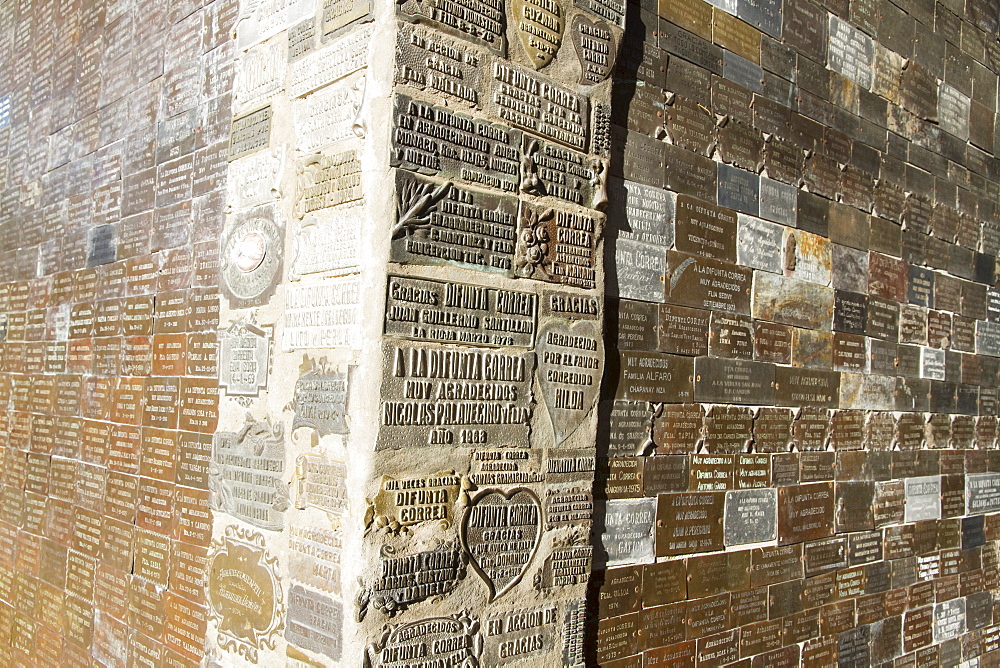 Thanksgiving plaques on a shrine at the Difunta Correa Sanctuary, Vallecito, San Juan, Argentina. La Difunta Correa is the most popular of Argentina's folk saints. She was a woman whose husband was forcibly recruited around the year 1840, during the Argentine civil wars. Becoming sick, he was then abandoned by partisans. In an attempt to reach her sick husband, Deolinda took her baby and followed the tracks of the partisans through the desert of San Juan Province. When her supplies ran out, she died. Her body was found days later by gauchos, however they found the baby still alive, feeding from the deceased woman's miraculously ever-full breast. Once the folk tale became known, her devout followers believe her to perform miracles and intercede for the living. Cattle keepers and truck drivers create small altars throughout Argentina and leave bottles of water as votive offerings.